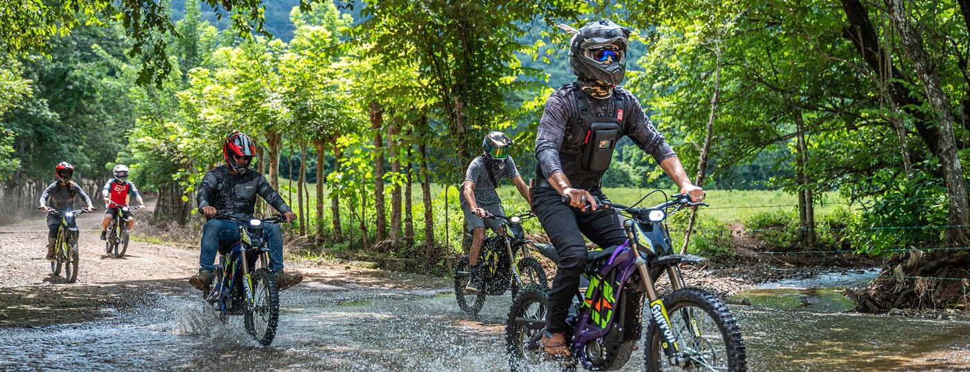 Electric dirt bike riders exploring a rainforest stream